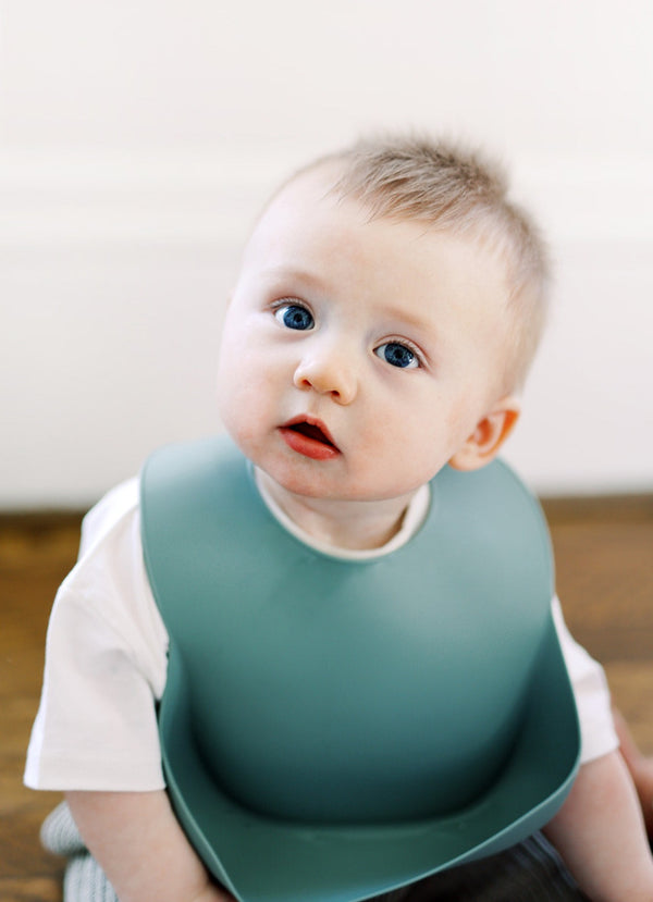 Baby boy staring up at camera wearing a forest green silicone baby bib