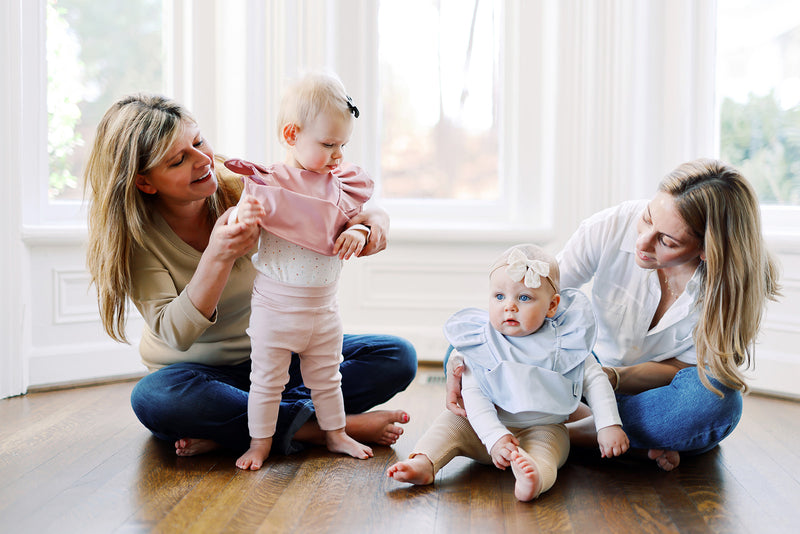 two moms with their baby girls wearing ruffle baby bibs