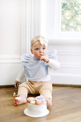 infant girl sitting and wearing a sky blue ruffle baby bib and eating cake