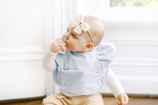 baby girl wearing a sky blue ruffle angel baby infant bib eating a cupcake