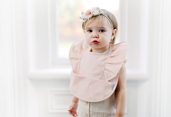Toddler girl wearing a peach blush ruffle angel baby bib