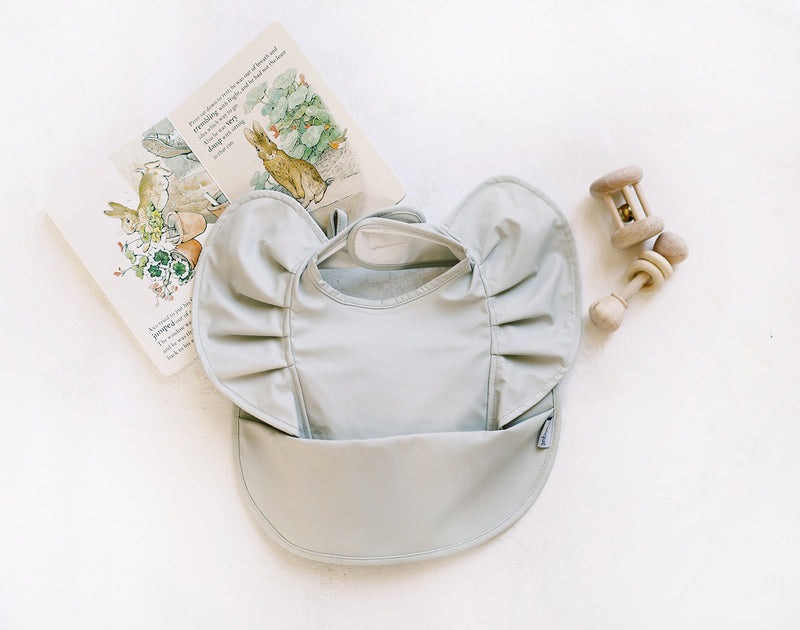 sage green ruffle baby bib with baby book and rattles
