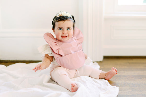 Baby girl sitting and wearing a pink blush ruffle baby bib
