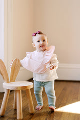 infant girl standing and wearing a pink ruffle baby bib