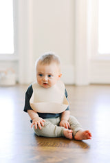 Baby boy sitting wearing an oat bibtique silicone baby bib